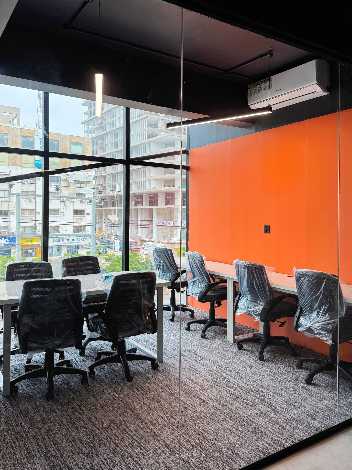 Shared desk workspace with orange accent wall and city view at WorkMore, The Pavilion